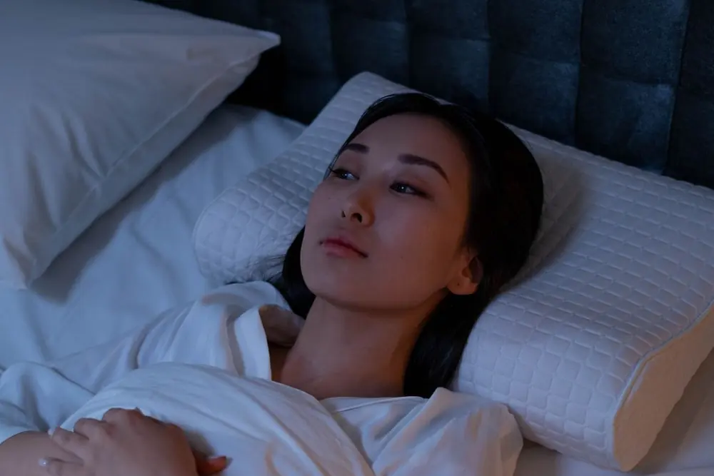Mulher deitada na cama, acordada no meio da noite